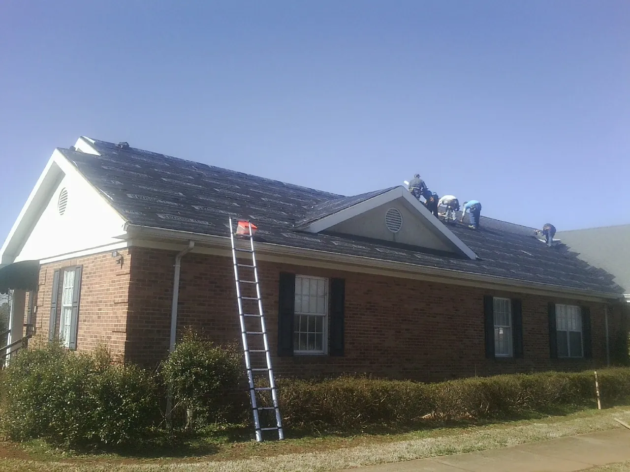 Crew tearing shingles off a brick ranch roof with a ladder set — Emergency Roof Repair work by our crew in Devon