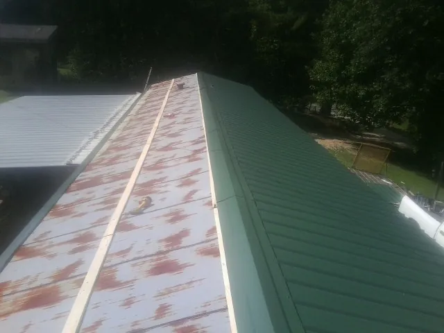 Old rusted panels beside newly installed green metal roofing — Wind Damage Roof Repair by Roofing Brothers in Devon