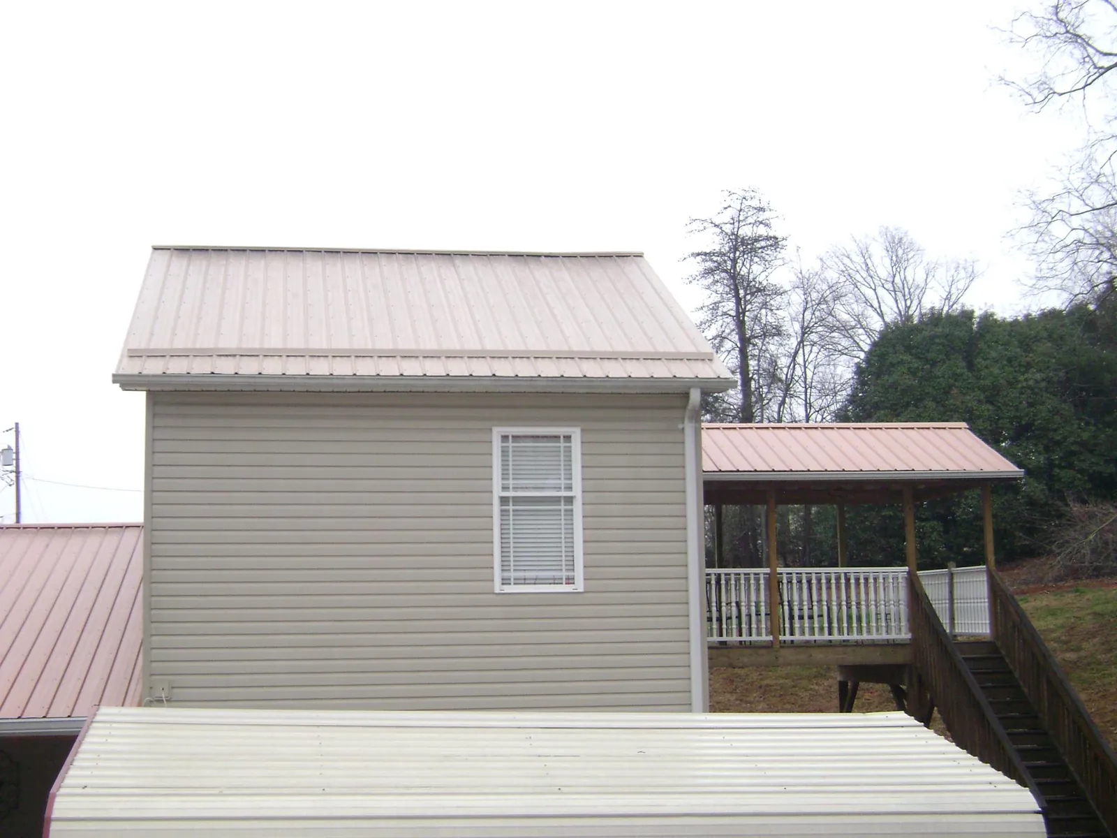 Tan metal roofs on a two story addition and attached porch, from a Roof Replacement job in Devon